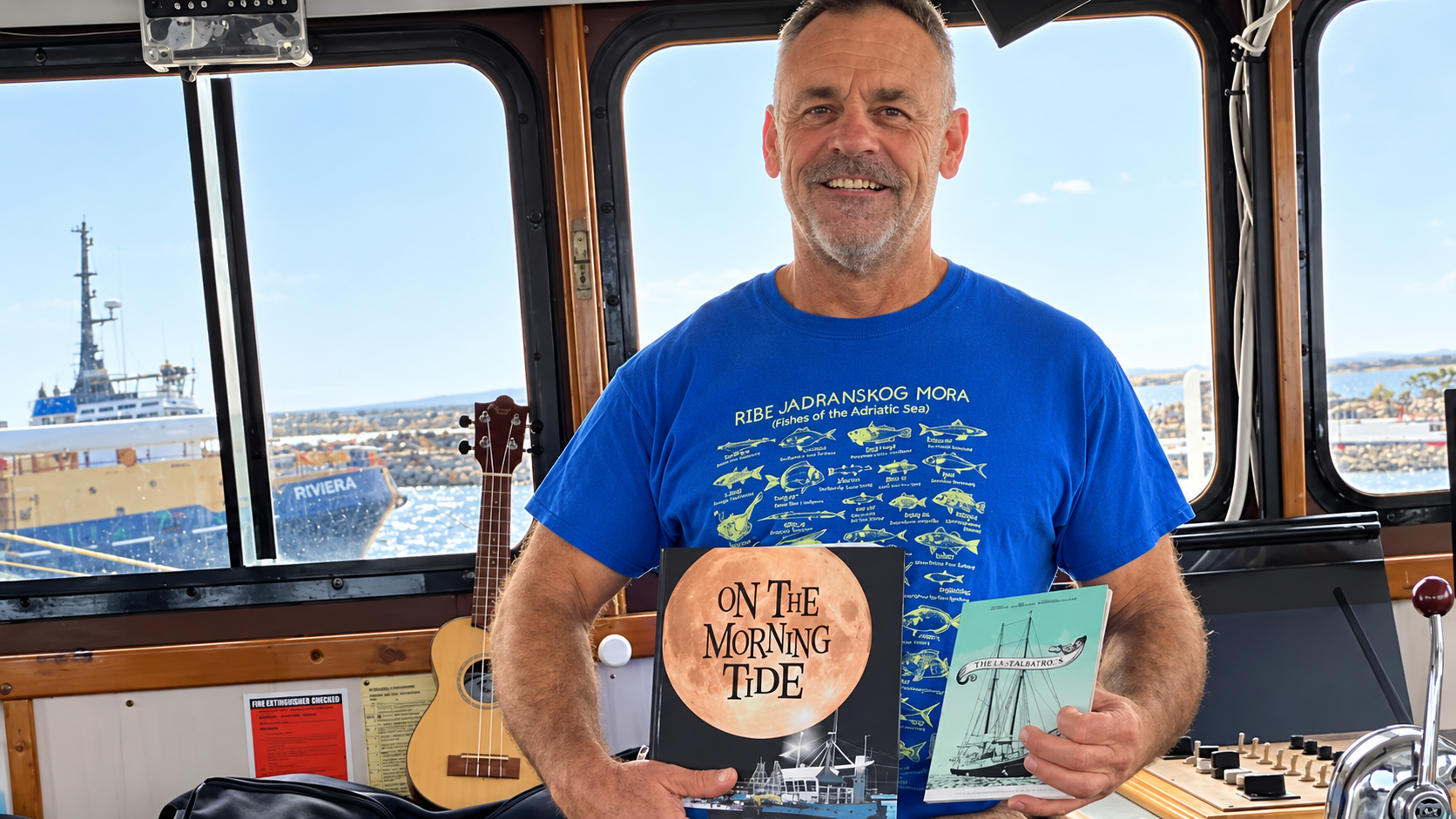 Peter Tudorovic aboard a fishing boat holding On the Morning Tide and The Last Albatross